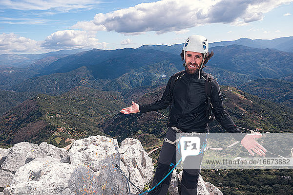 Konzept: Abenteuer. Bergsteiger Mann mit Helm und Gurtzeug. Auf dem Gipfel des Berges. Mit offenen Armen und lächelnd zeigt er die Landschaft. Via ferrata auf Felsen.