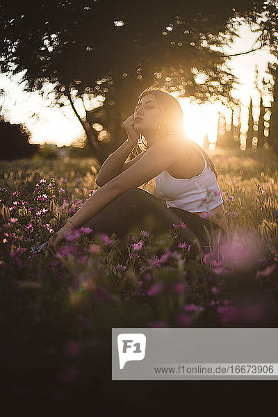 Langweiliger Teenager  der bei Sonnenuntergang auf einem Feld zwischen Blumen sitzt