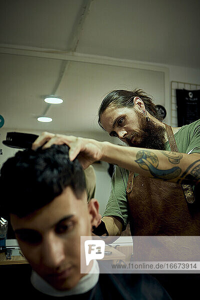 Ein Friseur  der sich auf das Schneiden der Haare eines Kunden konzentriert