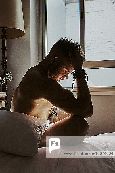 Ein junger nackter Mann sitzt auf dem Bett und hat starke Kopfschmerzen