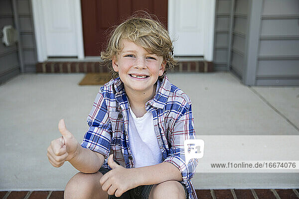 Toothless First Grade Boy Gives Thumbs Up While Sitting on Brick Steps