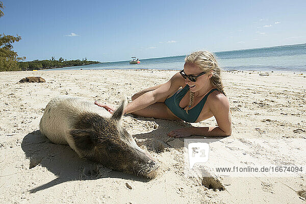 Glückliche junge Frau liegt mit einem Schwein im Sand am Strand während des Sommerurlaubs
