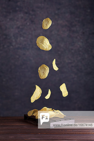 Kartoffelchips fallen in eine Tonschale auf grauem Hintergrund. Fliegende Chips in Großaufnahme.
