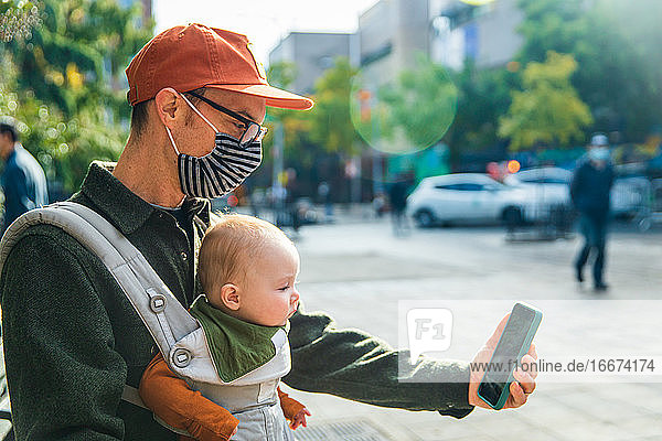 Vater mit kleiner Tochter führt während der COVID-19 auf der Straße Videotelefonate über sein Smartphone.