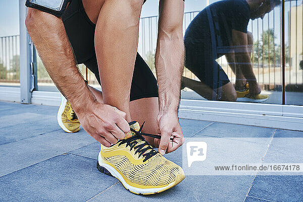 Sportsman tying his shoelaces. He is wearing yellow sneakers.