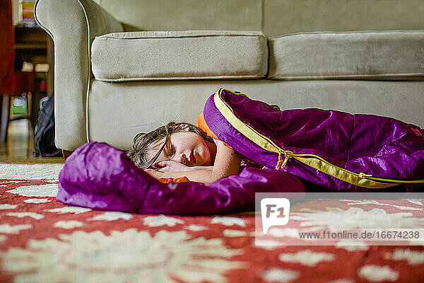 Ein hübsches kleines Mädchen liegt in einem Schlafsack auf dem Boden in einem Haus