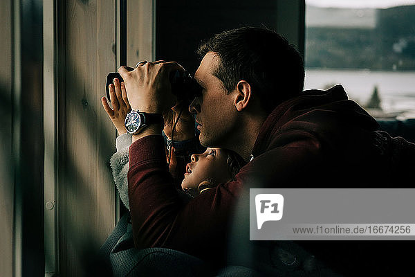 Vater und Tochter schauen mit dem Fernglas aus dem Fenster auf die Natur