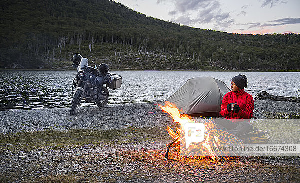 Woman enjoying campfire at camp next to still lake in Tierra del Fuego