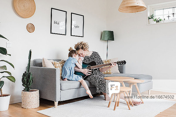 Mutter und Tochter kuscheln zu Hause beim Gitarrespielen