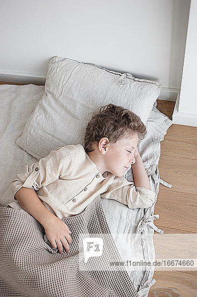 Junge in Leinenkleidung schläft tagsüber in einem mit Naturleinen bezogenen Bett.