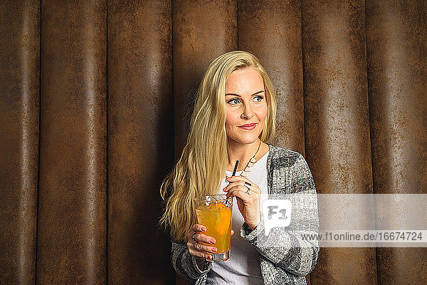 Erwachsene Frau mit Cocktail in der Nähe der Lederwand