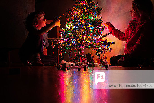 Kleine Kinder schmücken ihren Weihnachtsbaum bei Nacht