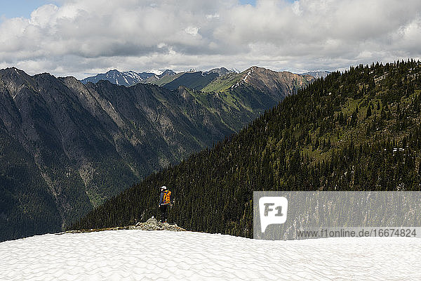 Einsame Wanderin mit Rucksack und Blick auf majestätische bewaldete Berge