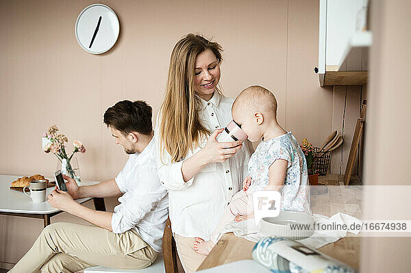 Mutter füttert ihr Kind am Küchentisch  während der Vater online chattet.
