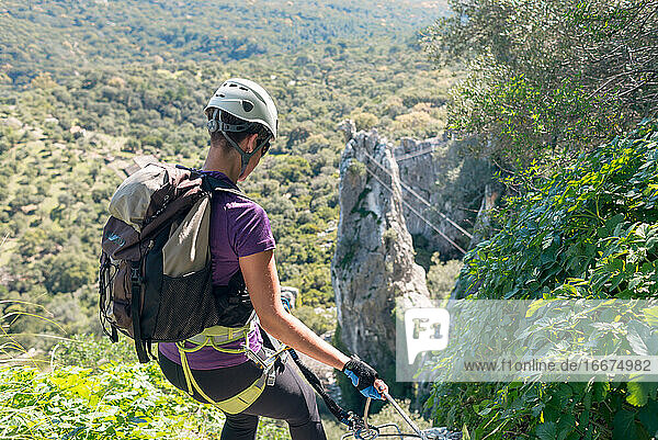 Adventure. Woman with helmet  harness and backpack. Descending in the mountains by a via ferrata.