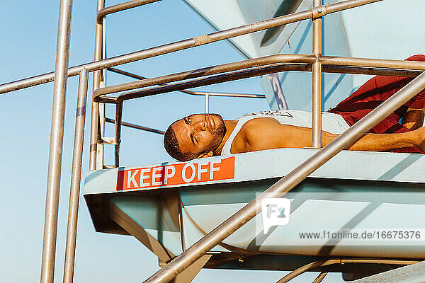 Porträt eines männlichen Sportlers  der sich auf einem Rettungsschwimmerturm ausruht