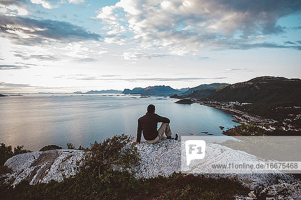 Mann sitzt auf einem Felsen mit Blick auf das Meer
