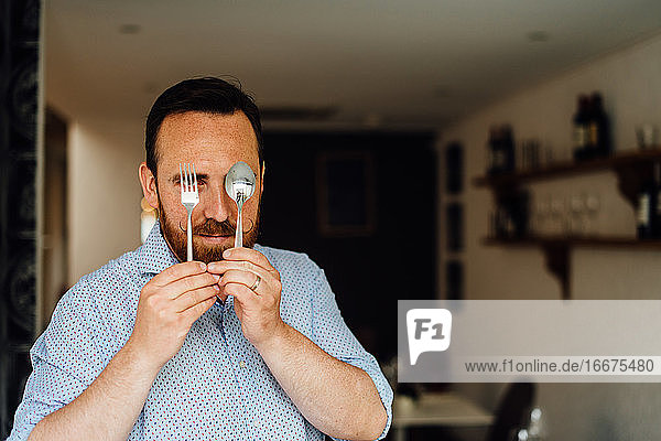 Man with moustache holding fork and spoon in front of his face