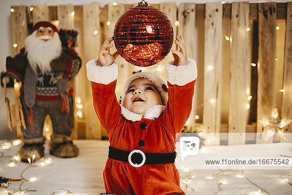 Ein als Weihnachtsmann verkleidetes kleines Mädchen versucht  eine Weihnachtskugel zu fangen
