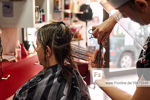 A close-up of a hairdresser cutting client's hair with a face shield