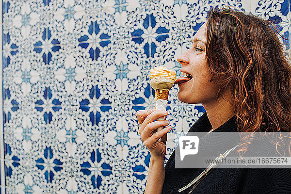 Junge Frau leckt Eis  während sie an einer gekachelten Wand in Lissabon steht