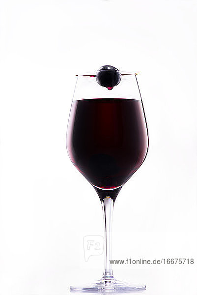 Wein tropft von einer roten Traube auf ein edles Glas Rotwein;