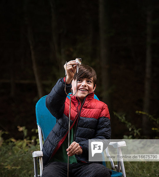 Kleiner Junge  der im Freien einen Marshmallow von einem Metallstab nimmt.