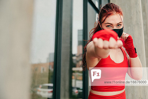 Young female boxer  training outdoors in Brooklyn wearing face-mask.