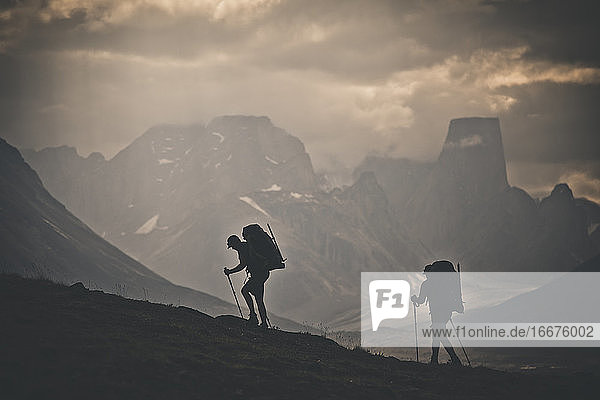 Silhouette of two backpackers hiking with rugged mountain view.