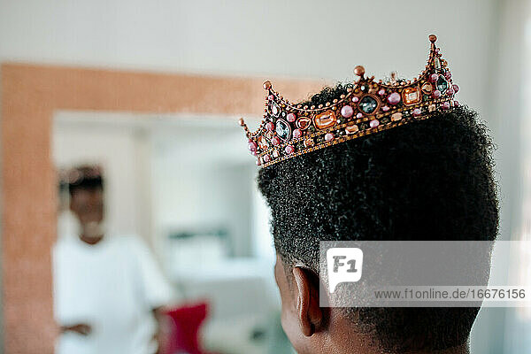 Afroamerikanischer Junge mit juwelenbesetzter Krone schaut in den Spiegel