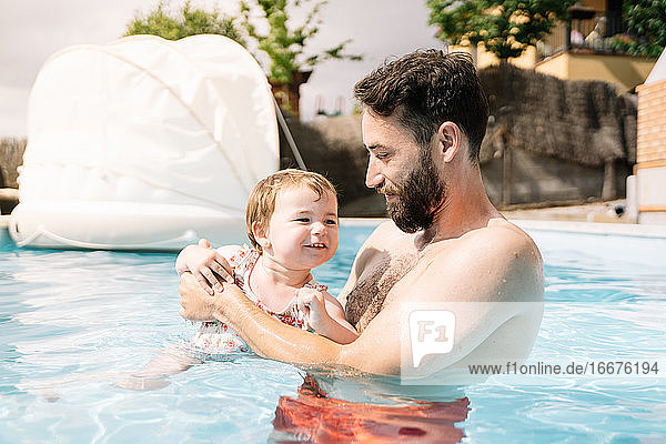 Man inside a house pool with a little girl in his arms swimming