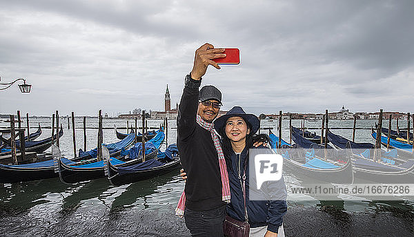 Thailändisches Paar macht ein Selfie vor einer geparkten Gondel in Venedig