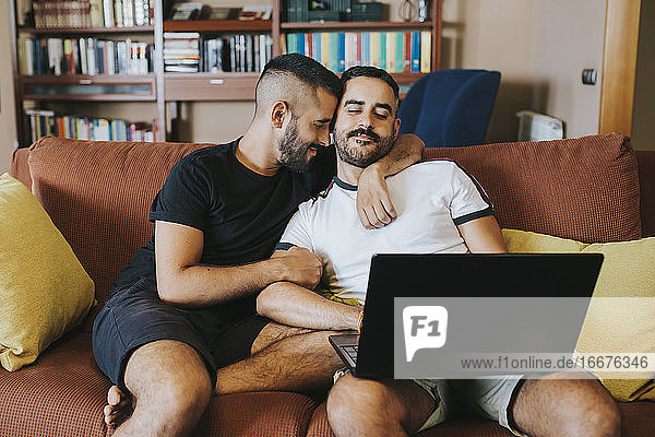 romantic gay couple using laptop on sofa