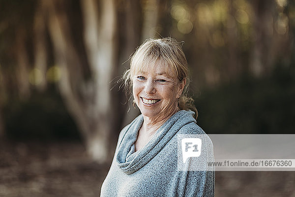 Porträt einer lächelnden älteren erwachsenen Frau  die im Wald lächelt