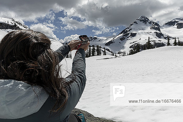 Unbekannte Reisende  die während einer Reise durch verschneite Berge an einem bewölkten Frühlingstag einen Kompass zur Navigation benutzt
