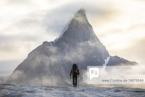 Rear view of backpacker approaching dramatic mountain.