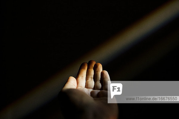 Unerkennbare weibliche Hand,  die sich in der Dunkelheit nach einem Regenbogen ausstreckt