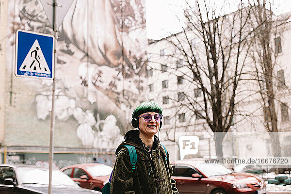 Happy hipster listening music in headphones walking on street in city