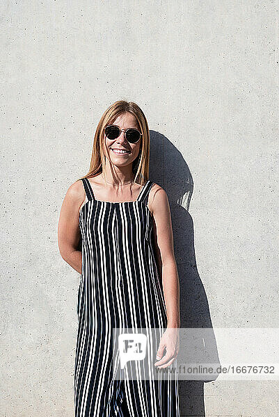 Lächelnde schöne junge Frau  die über einer Mauer steht und eine Sonnenbrille trägt