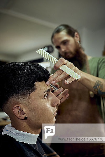A barber working with a comb and scissors on a young man