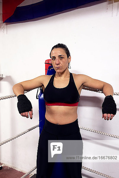 Echte weibliche Boxerin mit Handschuhen  die sich vor dem Training auf ein Seil im Ring stützt