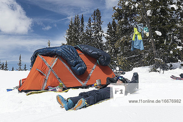 Junge Frau entspannt sich am Zelt auf einem schneebedeckten Berg