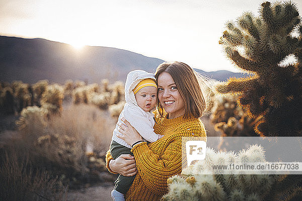 Eine Frau mit einem Baby steht in der Nähe eines Kaktus in der Wüste