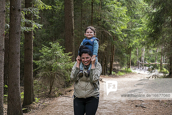 Portrait of smiling mother carrying son on shoulders while hikin