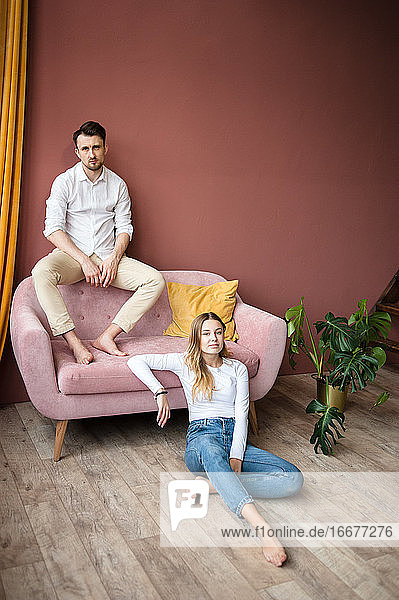 Ein Mann sitzt auf einem rosa Sofa mit dem Rücken zur Wand  eine Frau sitzt in der Nähe auf dem Boden.