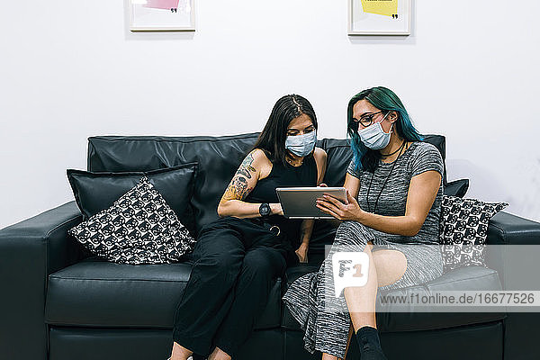 Zwei Geschäftsfrauen mit Masken benutzen in der Büropause ein Tablet