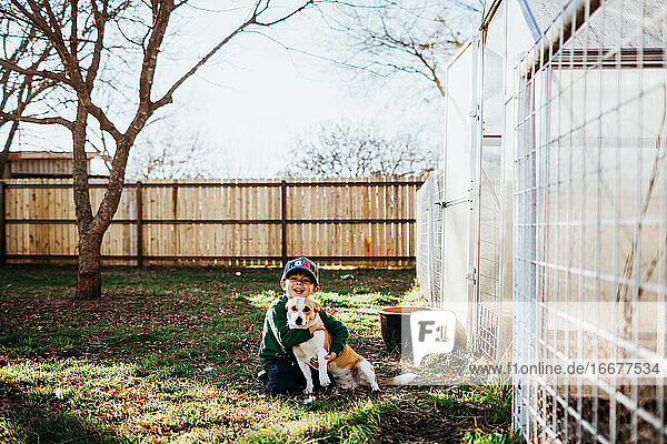 Junge lächelt und umarmt Hund im Hinterhof im Frühling