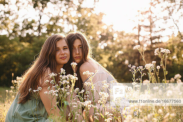 Portrait of lesbian couple sitting amidst flowers in summer forest