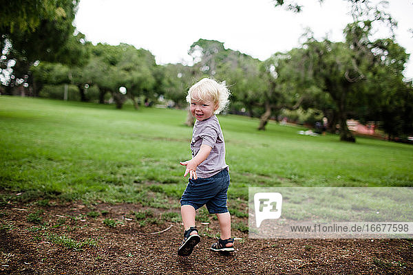 Zweijähriges Kind blickt beim Laufen durch den Park auf die Kamera zurück