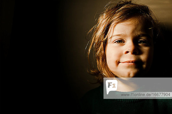 Determined toddler girl standing in bright light smiling